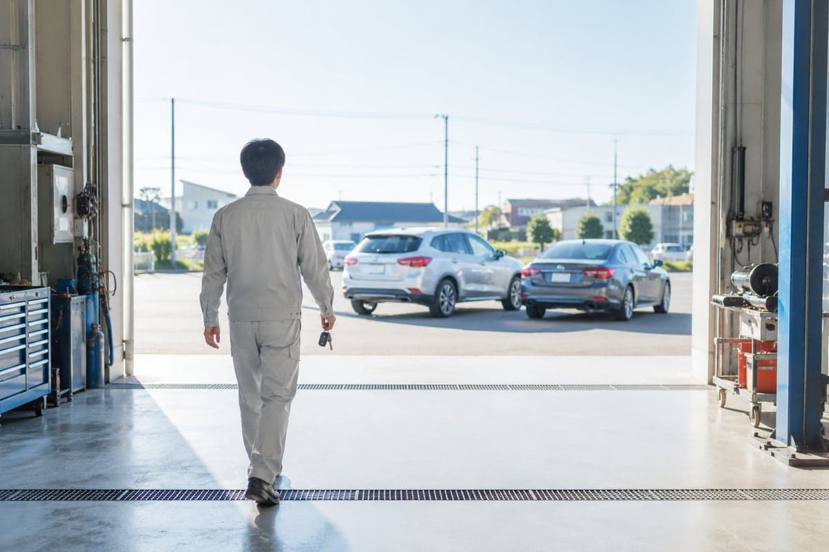 朝の整備工場から、鍵を持って屋外に停めた車へ向かうスタッフ